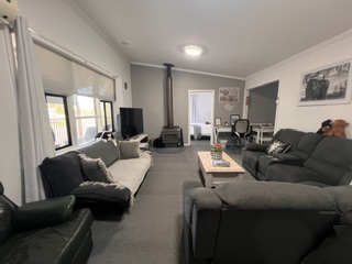 Open-plan lounge with wood heater, large corner lounges and TV in the 3 bedroom cottage